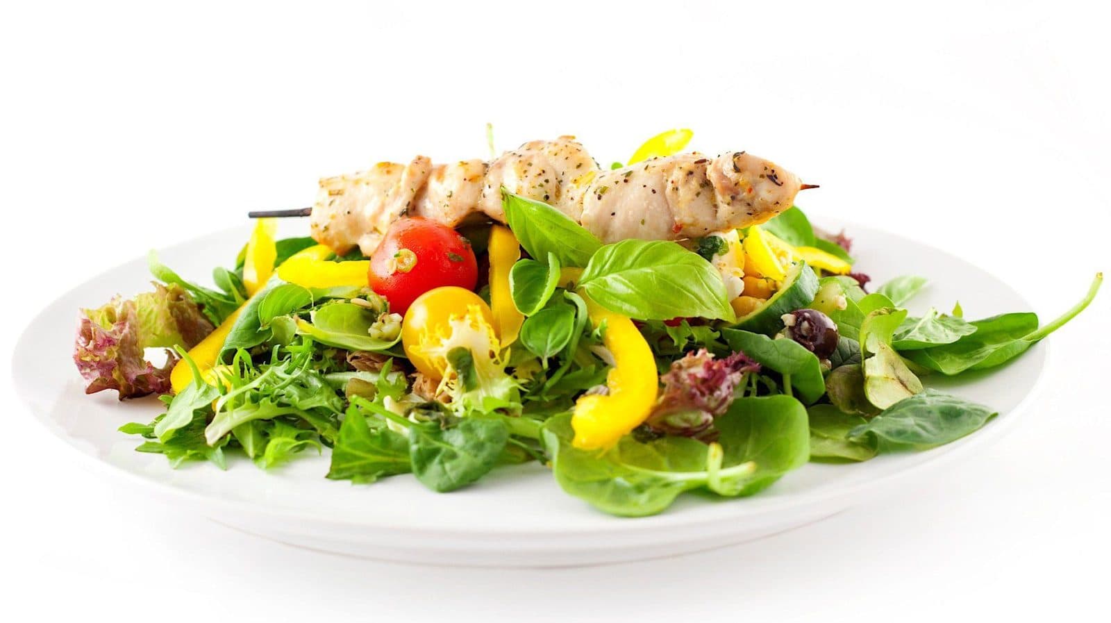 Ensalada de pollo a la parrilla con hojas verdes y pimientos en un plato blanco